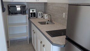 Een kleine keuken met witte kastjes, een roestvrijstalen koelkast, een magnetron, een koffiezetapparaat en een broodrooster.