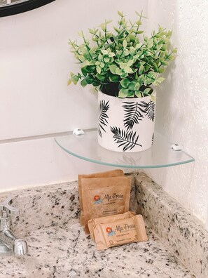 A bathroom with a granite countertop, a glass shelf, a potted plant, and two brown paper bags labeled 'Alfa Praia.' - Mirante Clube - Praia do Futuro (Fortaleza)