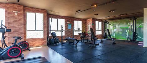 Un gimnasio con equipo de ejercicio, ventanas amplias y una pared de ladrillo.