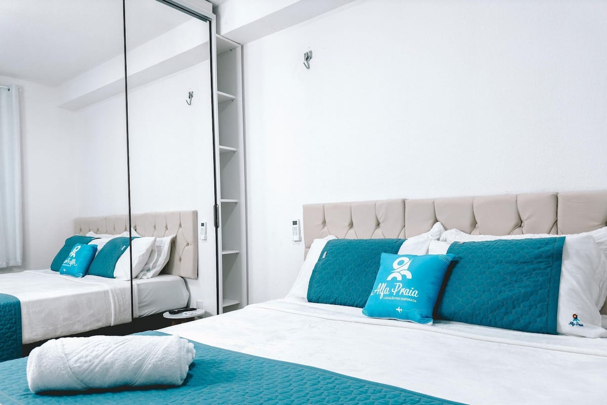 A hotel room with two beds, a minibar, a bathroom with a shower, and a large mirror.