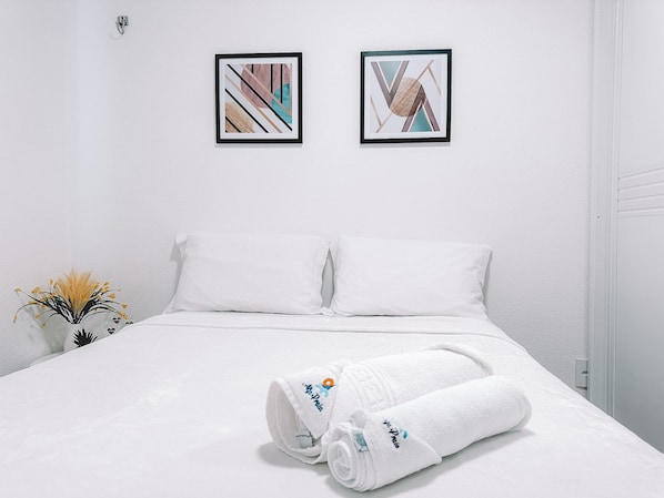 A hotel room with a neatly made bed, two framed abstract artworks on the wall, and a small potted plant on the nightstand.