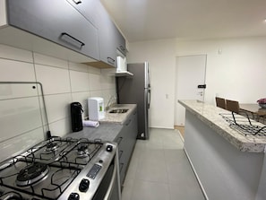 A kitchen with a gas stove, a coffee maker, a refrigerator, and a dining area with chairs.