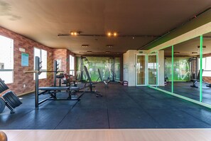 A gym with weightlifting equipment, mirrored walls, and a brick wall. - Mirante Clube - Praia do Futuro (Fortaleza)