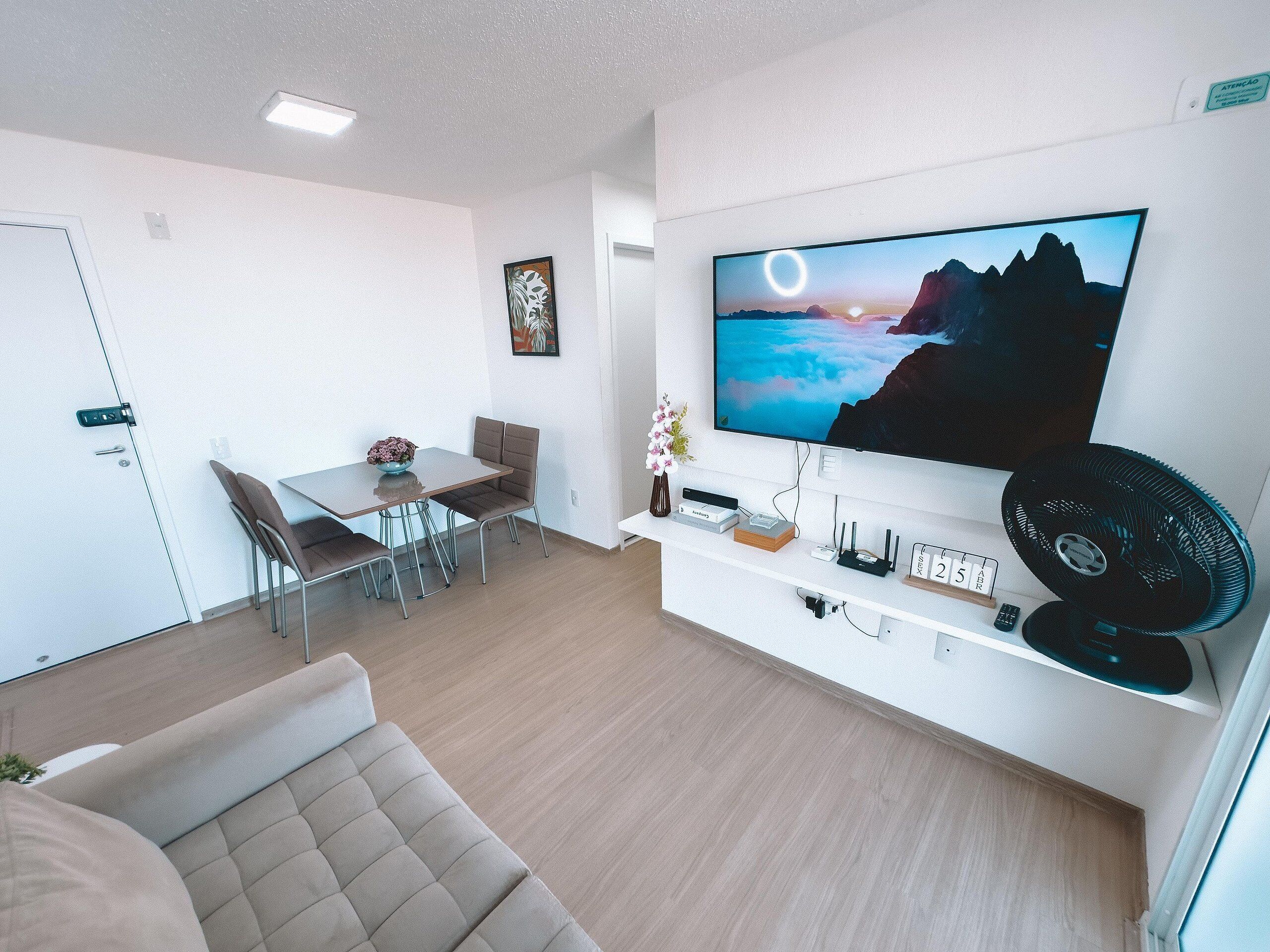 Una sala moderna con una televisión de pantalla plana, un sofá, un comedor con sillas y una pequeña mesa con un florero.