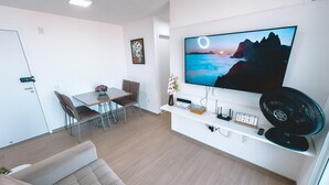 Een moderne woonkamer met een flatscreen televisie, een bank, een eethoek met stoelen en een kleine tafel met een vaas.