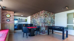A room with a pool table, a dining area with chairs, a kitchen in the background, and a wall with beer bottle labels. - Mirante Clube - Praia do Futuro (Fortaleza)