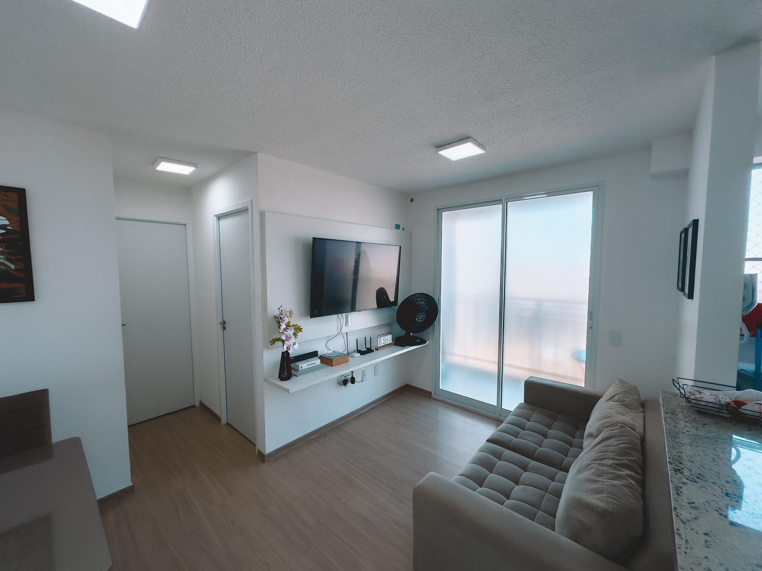 A modern living room with a flat-screen TV, a sofa, a coffee table, and a sliding glass door leading to a balcony.