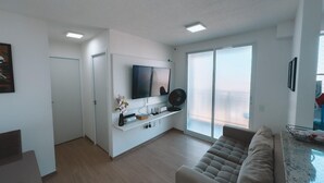 Een moderne woonkamer met een flatscreen televisie, een bank, een salontafel en een schuifpui naar een balkon.