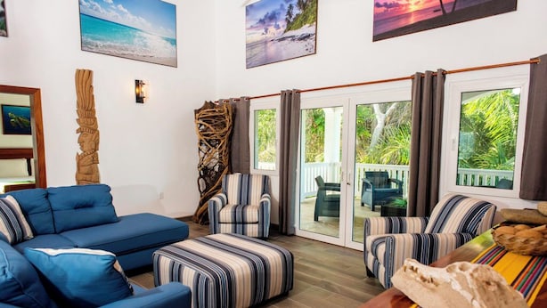 Una sala de estar con un sofá azul, sillones a rayas, una mesa de centro de madera y vistas al exterior a través de puertas de cristal amplias.