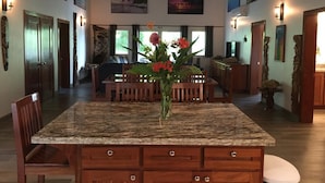 Un amplio comedor con una isla de granito, sillas de madera y un jarrón con flores.