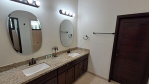 A bathroom with two sinks, a large mirror, vanity lights, and a dark wooden door.