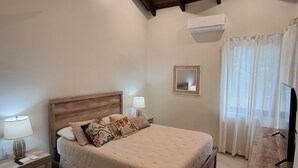 A bedroom with a wooden bed, bedside tables, a ceiling fan, an air conditioning unit, a mirror, and a TV.