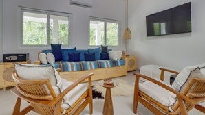 A modern living room with a sofa, two wooden chairs, a small round table, and a television mounted on the wall.