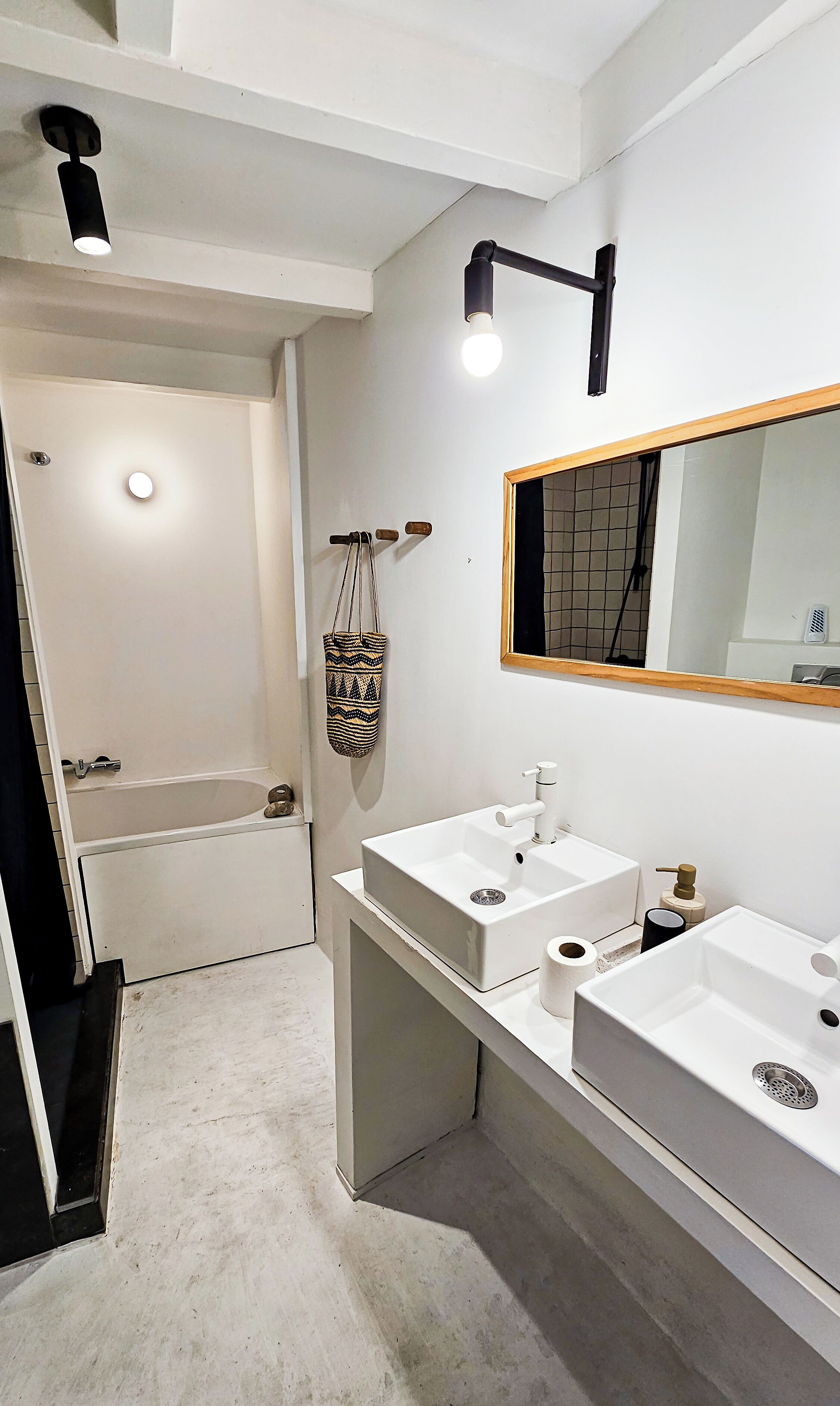 A modern bathroom with a bathtub, two sinks, a mirror, and a hanging bag.