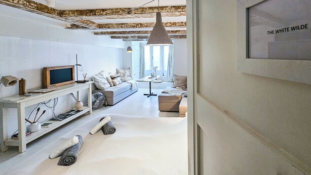 Una sala de estar moderna con un sofá, una mesa de centro y un televisor. Hay un ventilador en el suelo y una lámpara colgante.