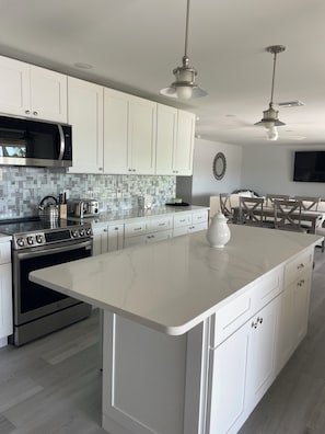 A modern kitchen with white cabinets, a large island, stainless steel appliances, and pendant lighting.