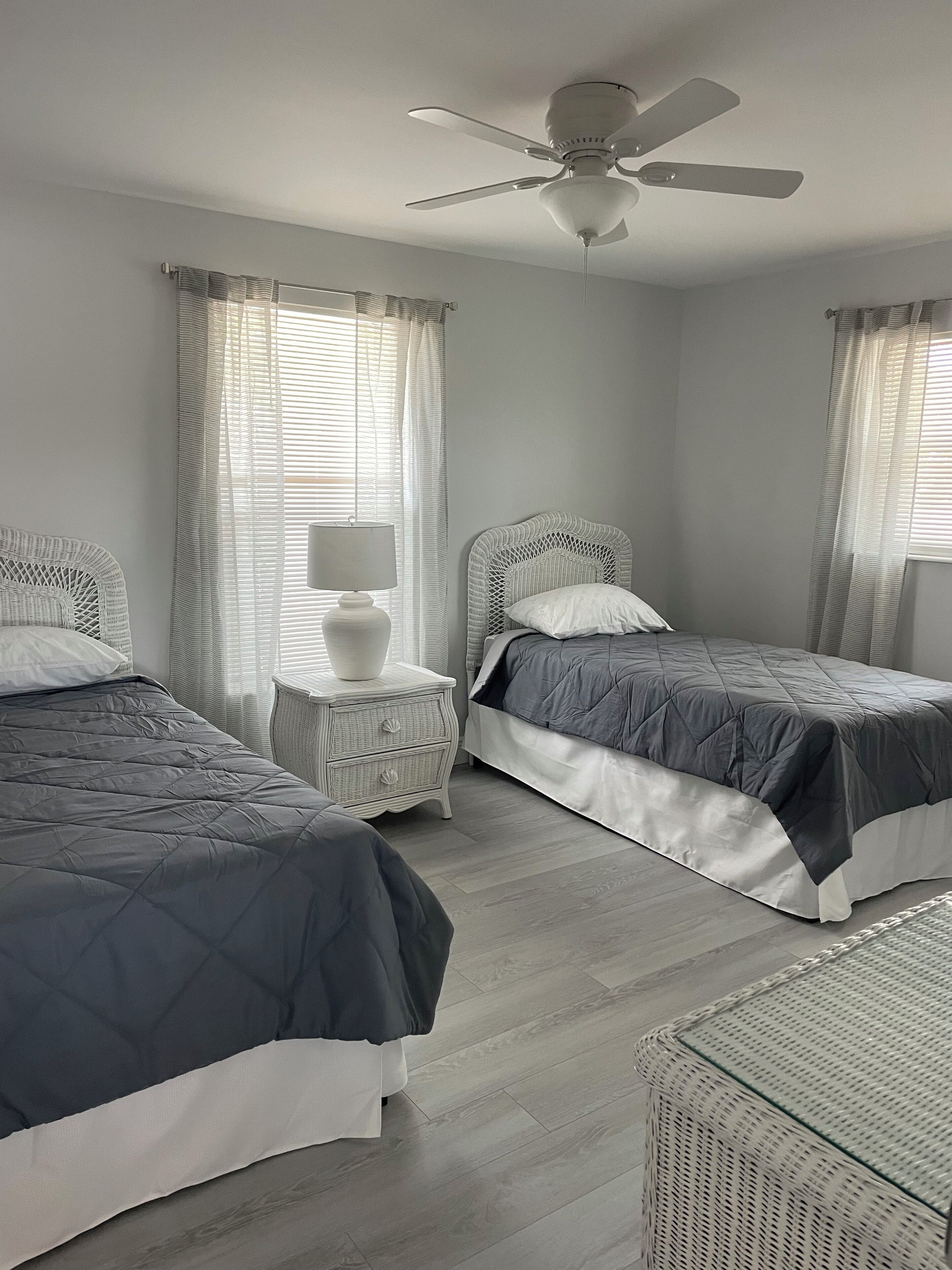 A bedroom with two beds, a ceiling fan, and a nightstand with a lamp.