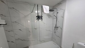 Un baño moderno con ducha de vidrio, azulejos de mármol blanco y un inodoro.