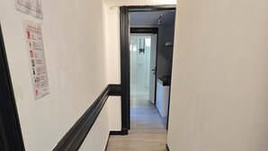 Un pasillo con suelo de madera y paredes blancas que conduce a un baño con cabina de ducha de vidrio.
