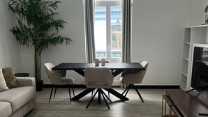 A modern living room with a dining area, featuring a large window, a potted plant, and a sofa.
