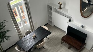 A modern living room with a dark wooden dining table, beige sofa, and a TV stand.