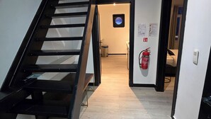 A staircase leading to a bedroom with a bed, a fire extinguisher, and a small window with a view.