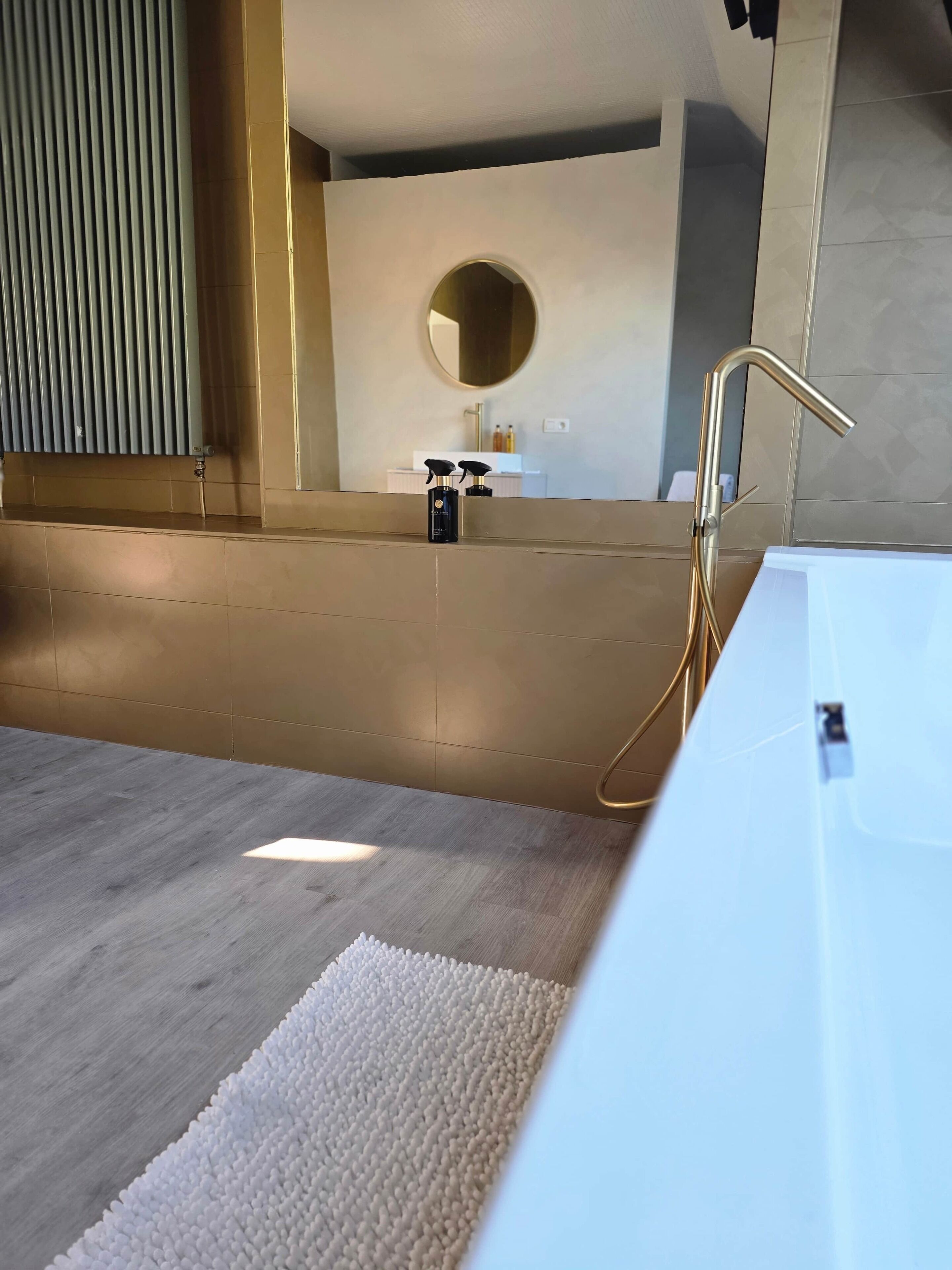 A modern bathroom with a large bathtub, a white sink, and a gold faucet.