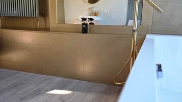A modern bathroom with a large bathtub, a white sink, and a gold faucet.