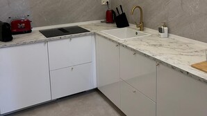 Una cocina moderna con armarios blancos, encimera de mármol, grifo dorado y tostadora roja.