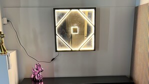 Una sala de estar moderna con piso de madera, una consola negra con diseño geométrico, un televisor montado en la pared y una escultura decorativa rosa.