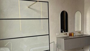 Habitación de hotel moderna con un espejo grande, dos camas, una tocador con lavamanos y un separador de vidrio.