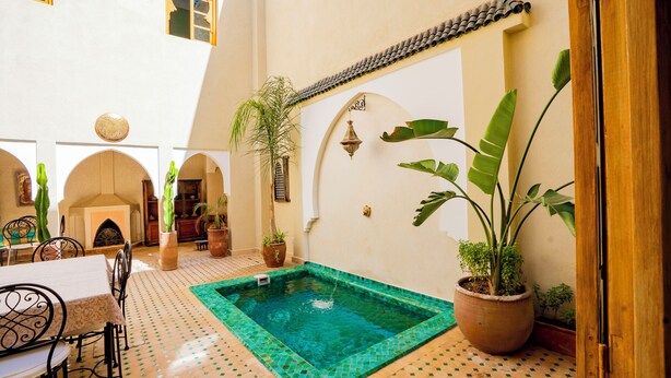 A courtyard with a swimming pool, potted plants, and a traditional Moroccan architectural style.