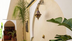 A swimming pool with a tiled edge, surrounded by potted plants and a wall with a decorative light fixture.