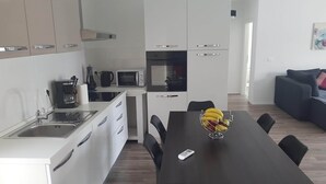 A modern kitchen with white cabinets, a black countertop, and a dining area with a black table and chairs.
