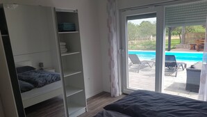A bedroom with a bed, a wardrobe, and a sliding glass door leading to a pool area.