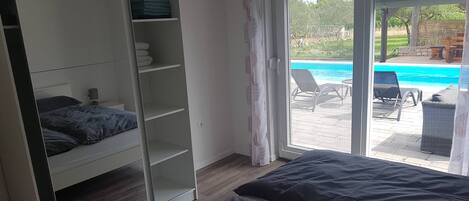 Ein Schlafzimmer mit Bett, Kleiderschrank und einer Schiebetür zu einem Poolbereich.