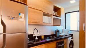 A modern kitchen with a stainless steel refrigerator, wooden cabinets, a microwave, a stove, and a washing machine.