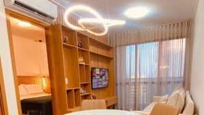 A modern living room with a round dining table, two chairs, a sofa, a TV, and a built-in bookshelf.