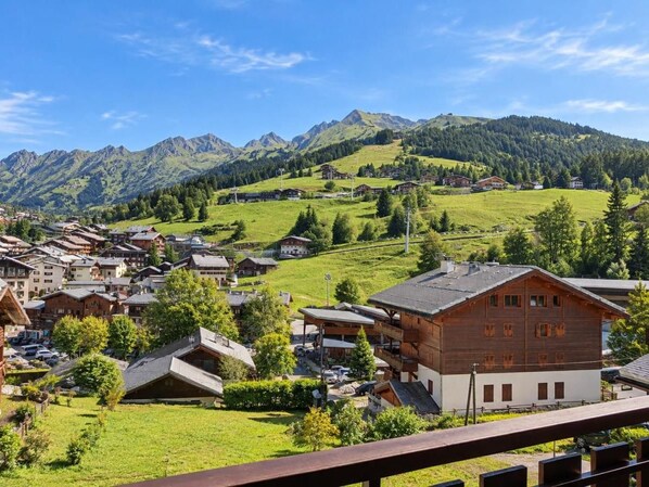 A mountain village with traditional wooden houses, a prominent chalet, and a view of the surrounding hills.