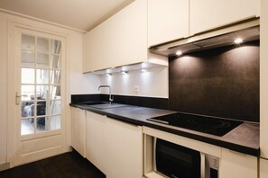 A modern kitchen with a black countertop, stainless steel appliances, and a window with frosted glass.