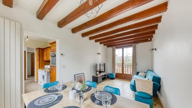 Un comedor con una mesa de madera dispuesta para cuatro personas, un sofá azul y una cocina al fondo.