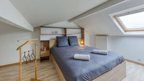 Un dormitorio con tragaluces, una cama con cabecera, una mesita de noche y un tendedero de madera.