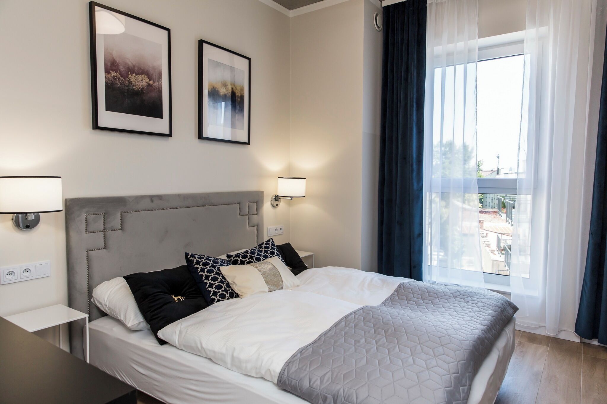 A modern hotel room with a large bed, two bedside lamps, and two framed pictures on the wall.