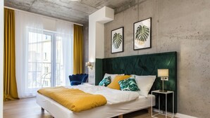A modern bedroom with a large bed, a green headboard, and tropical leaf wall art. - Piedmont House (Kraków)