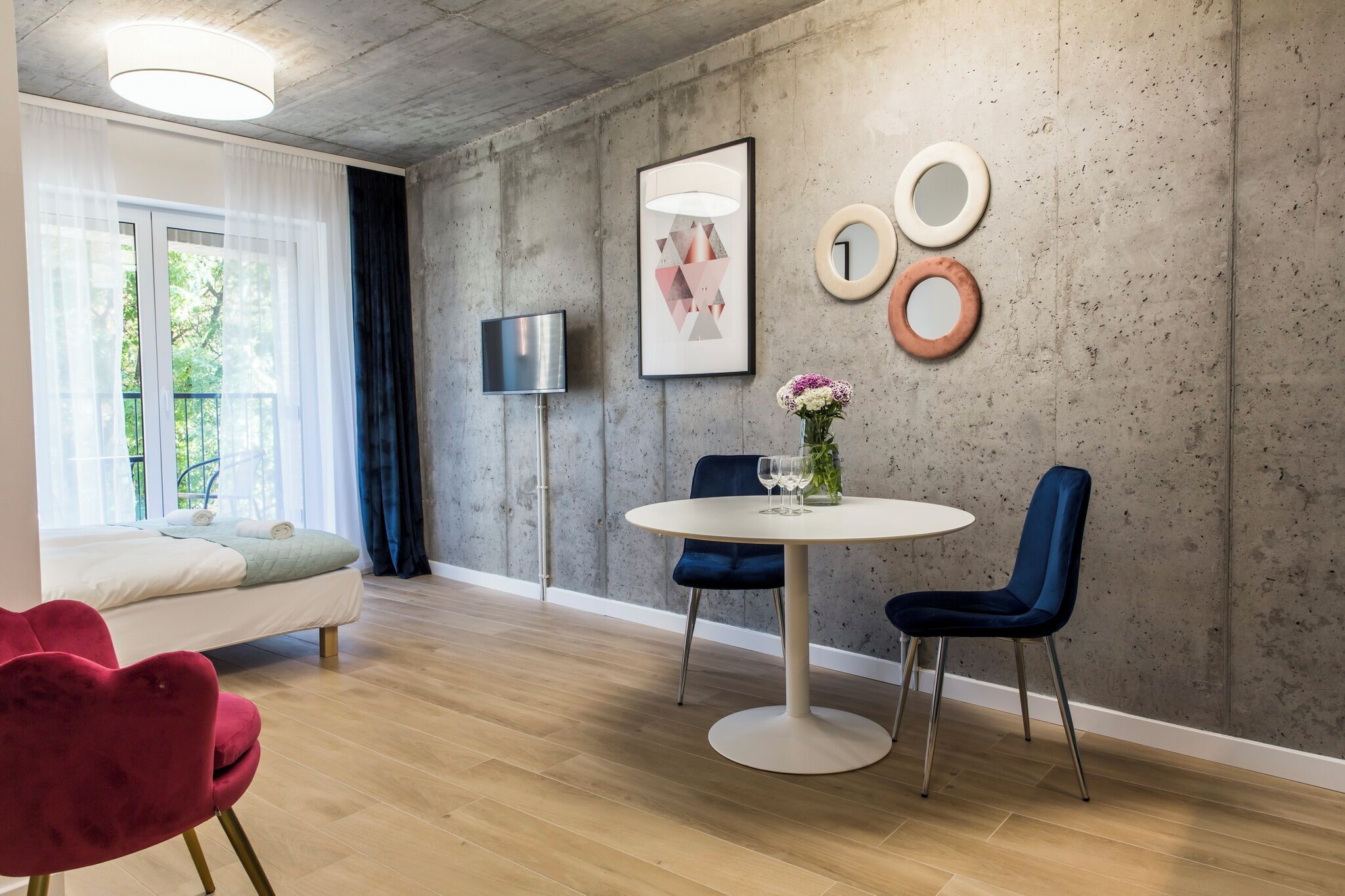 A modern living room with a sofa, a round dining table, and two chairs. A TV is mounted on the wall, and there are decorative items on the wall.