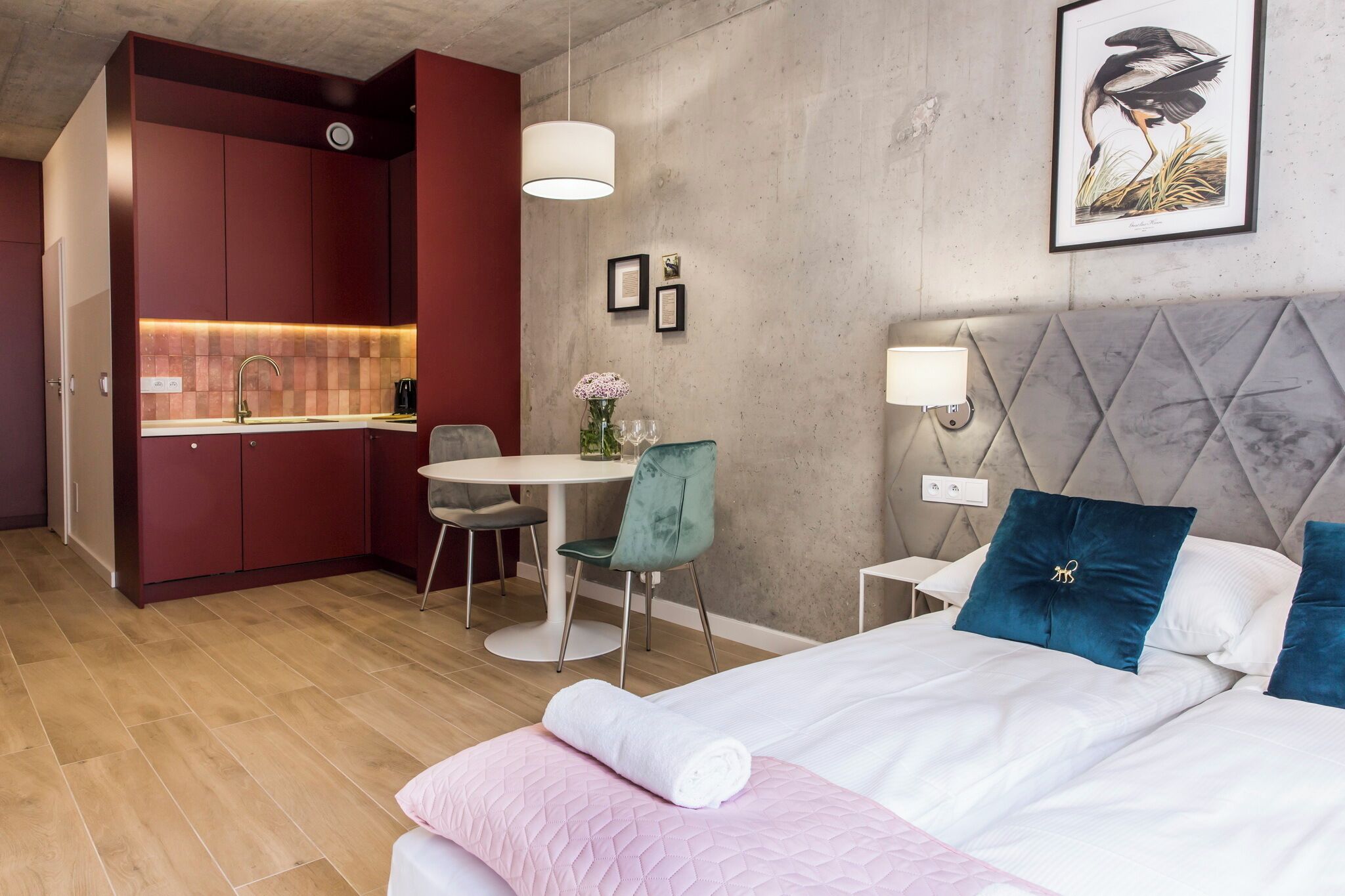 A compact hotel room with a kitchenette, a dining area, and a bed with decorative pillows.