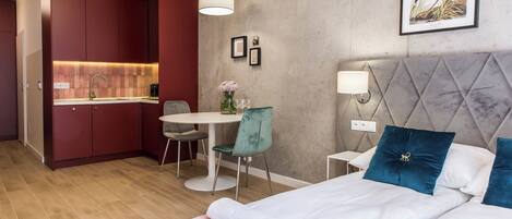 A compact hotel room with a kitchenette, a dining area, and a bed with decorative pillows.