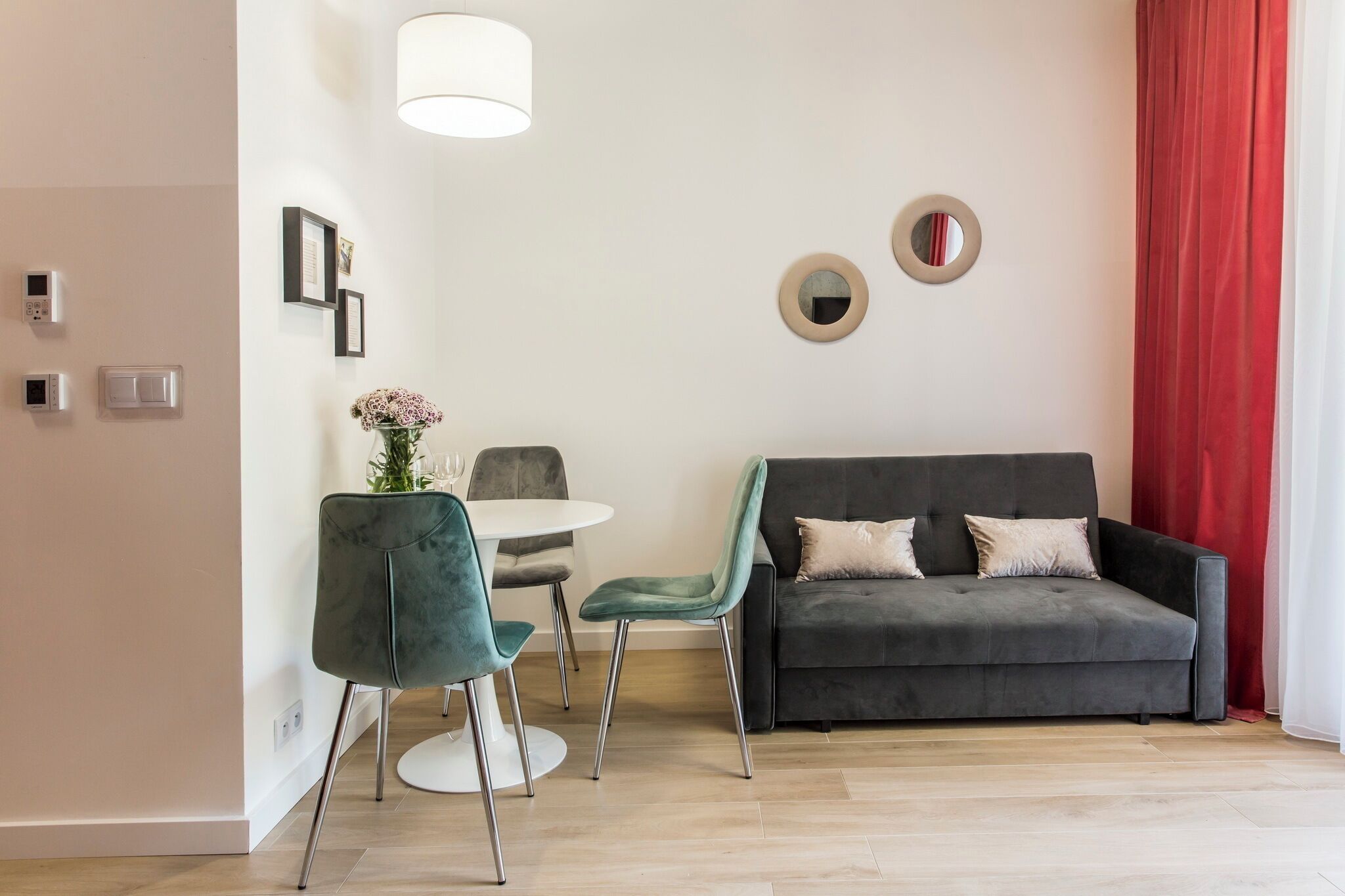 A modern living room with a grey sofa, teal chairs, a small round table, and a vase of flowers.