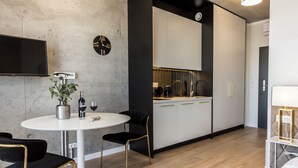 A modern kitchen with white cabinets, a black clock, and a flat-screen TV mounted on the wall. - Piedmont House (Kraków)