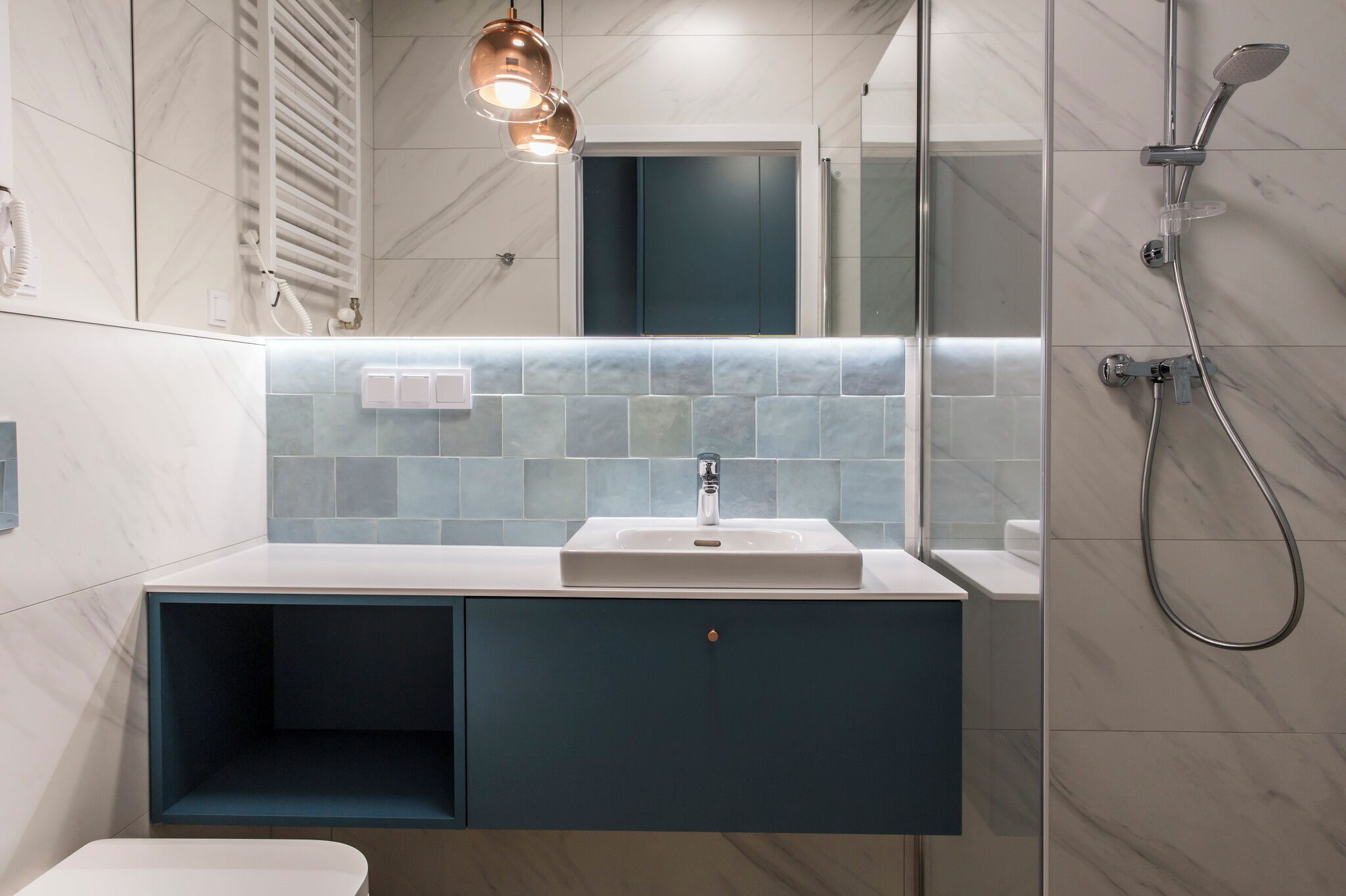 A modern bathroom with a white sink, a towel rack, and a shower.